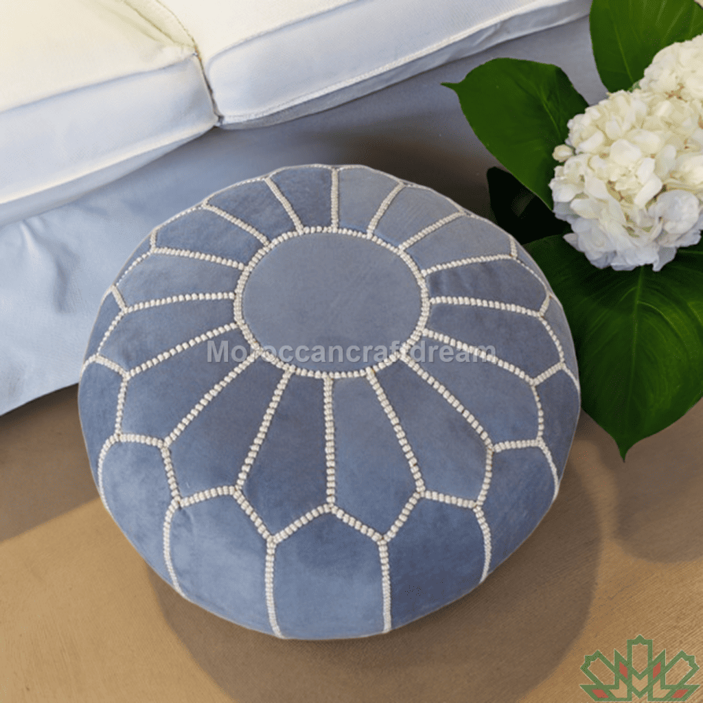 Blue patterned ottoman on a wooden floor with a white flower arrangement in the background.