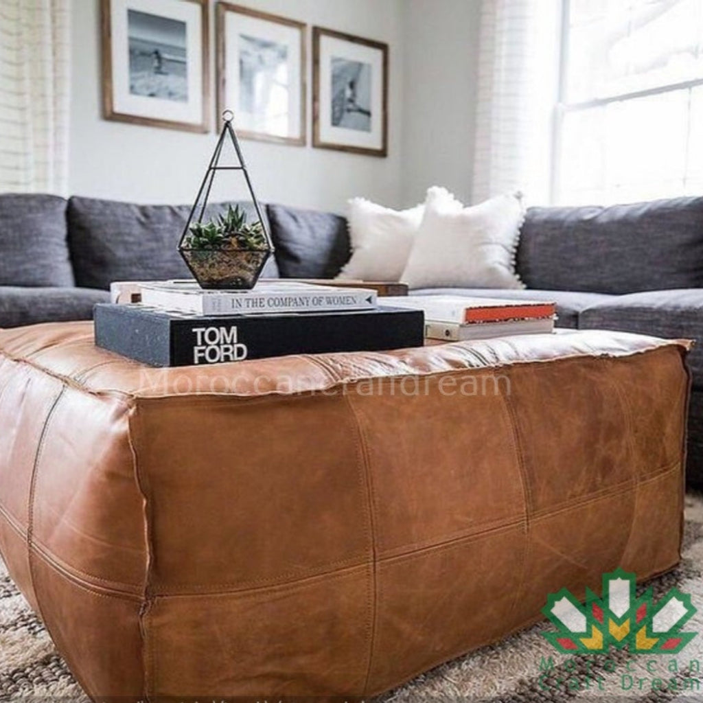 Brown leather ottoman in a living room with books and decor items.