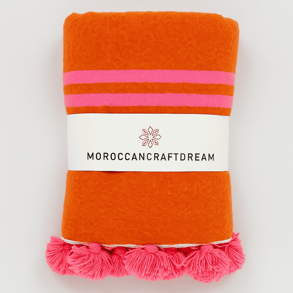 Orange towel with pink stripes and tassels, featuring a 'Moroccancraftdream' label on a white background.