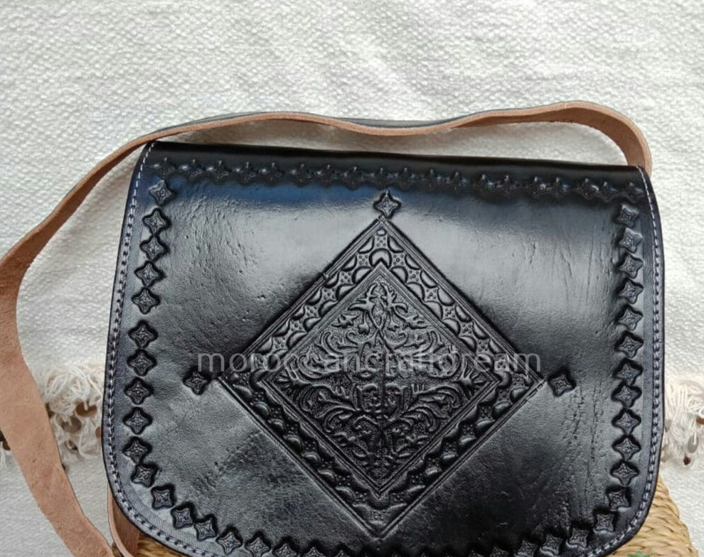A handmade black leather bag with intricate embossed patterns and a shoulder strap.