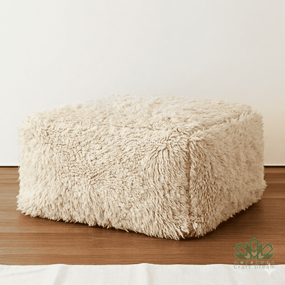 Beige cube-shaped ottoman on a wooden floor with a white wall background