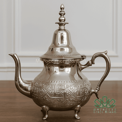 Silver teapot with intricate designs on a wooden surface