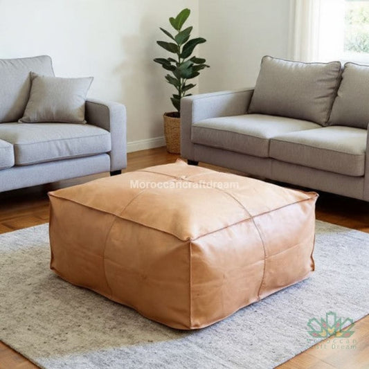 Natural beige leather ottoman in a living room with gray sofas and a plant.