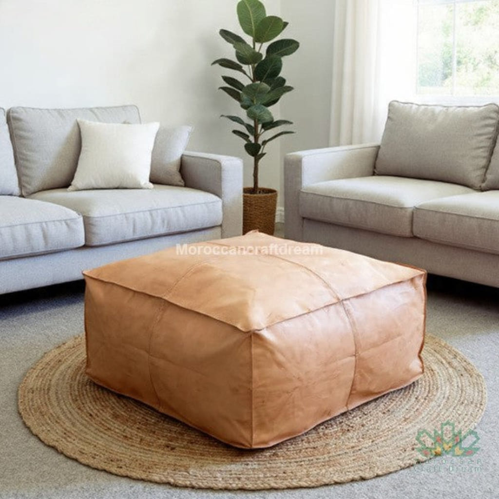 Natural beige leather pouf in a living room setting with beige sofas and a plant.