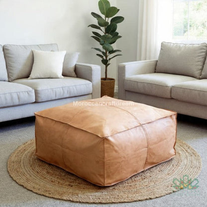 Natural beige leather pouf in a living room setting with beige sofas and a plant.