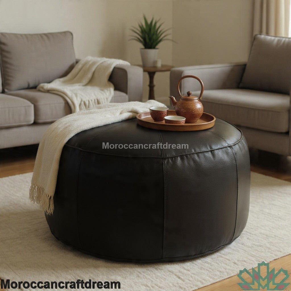 Round black leather ottoman in a living room setting with a tray of tea and a blanket.