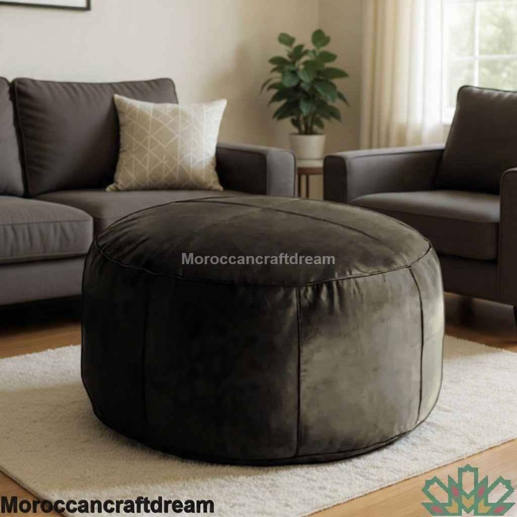 Round dark gray ottoman in a living room setting with a sofa and plant.