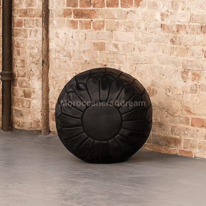 Black leather pouf against a brick wall