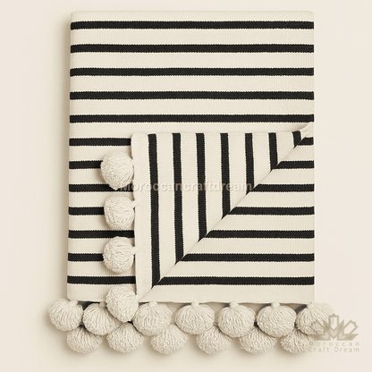 Black and white striped blanket with pom-pom trim on a beige background