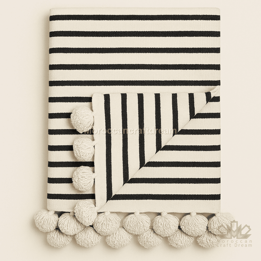 Black and white striped blanket with pom-pom trim on a beige background