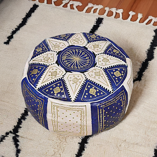 A handcrafted blue and white leather Moroccan pouf ottoman placed on a beige textured rug.