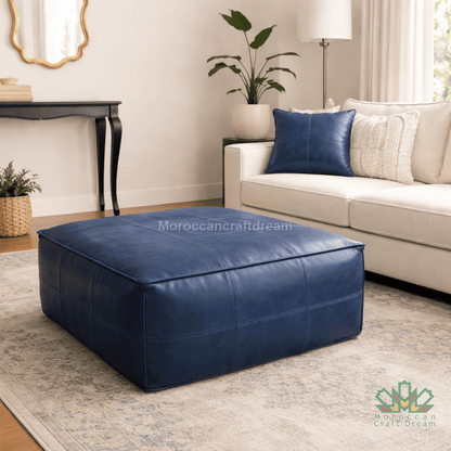 Blue leather ottoman and leather pillow in a living room setting with a beige sofa and decorative items.