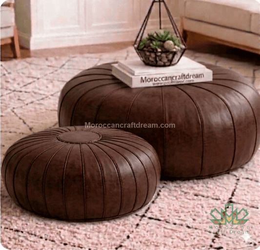 Two brown leather ottomans on a patterned rug with a small plant and book on top.
