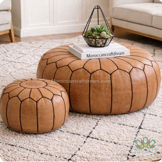 Two caramel leather poufs with black stitching on a textured rug with a small plant and book on top.