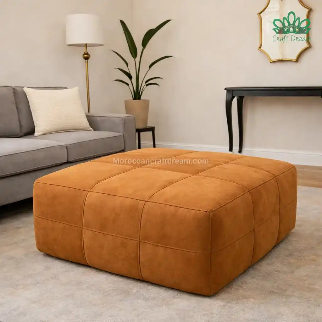 Caramel sude leather ottoman in a living room setting with a gray sofa and plant.