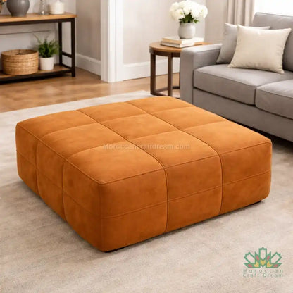 Caramel suede leather ottoman in a living room setting with a gray sofa and wooden coffee table.