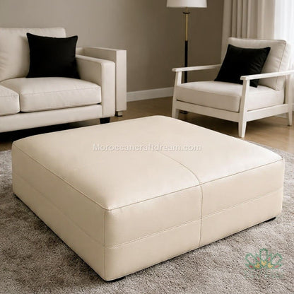 Beige leather ottoman in a living room setting with two matching chairs.