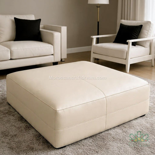 Beige leather ottoman in a living room setting with two matching chairs.