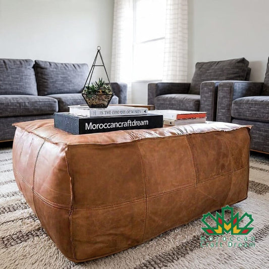 Darky light caramel leather ottoman in a living room with books and decor items.
