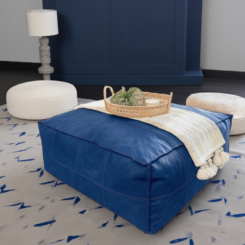 Blue ottoman with a blanket and basket on a patterned rug, with a lamp and cushions in the background.