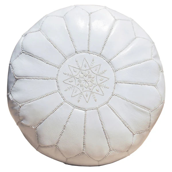 A handcrafted brown Moroccan leather ottoman with white stitching on a red carpet.