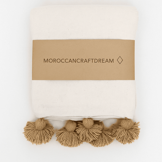 Decorative hadnmade white blanket with brown pompoms tassels and 'Moroccancraftdream' branding on a white background