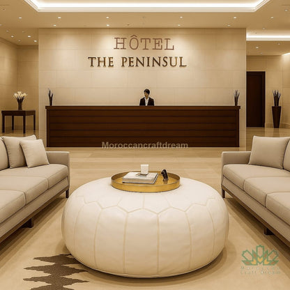 Hotel reception area with 'The Peninsula' sign and beige interior design and white leather ottoman.