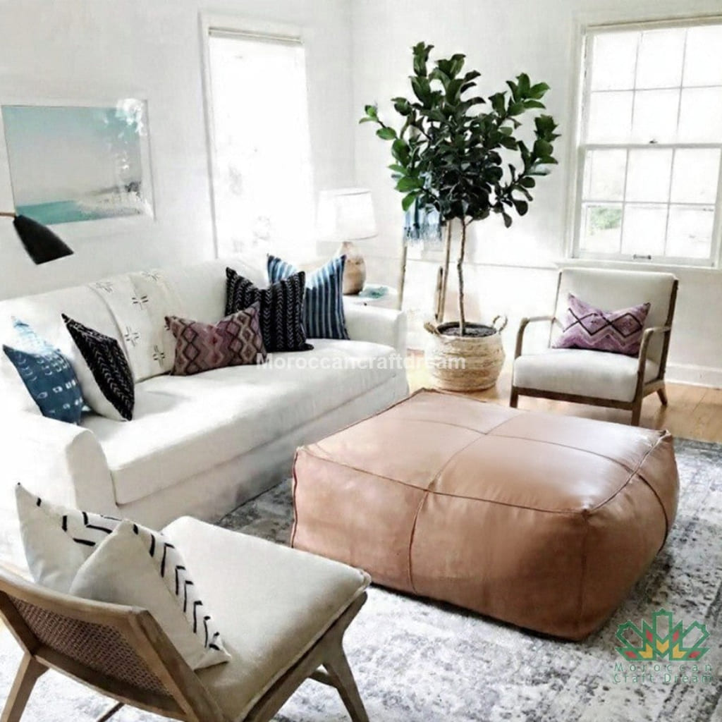 Living room with a white sofa, brown leather ottoman, and decorative pillows.