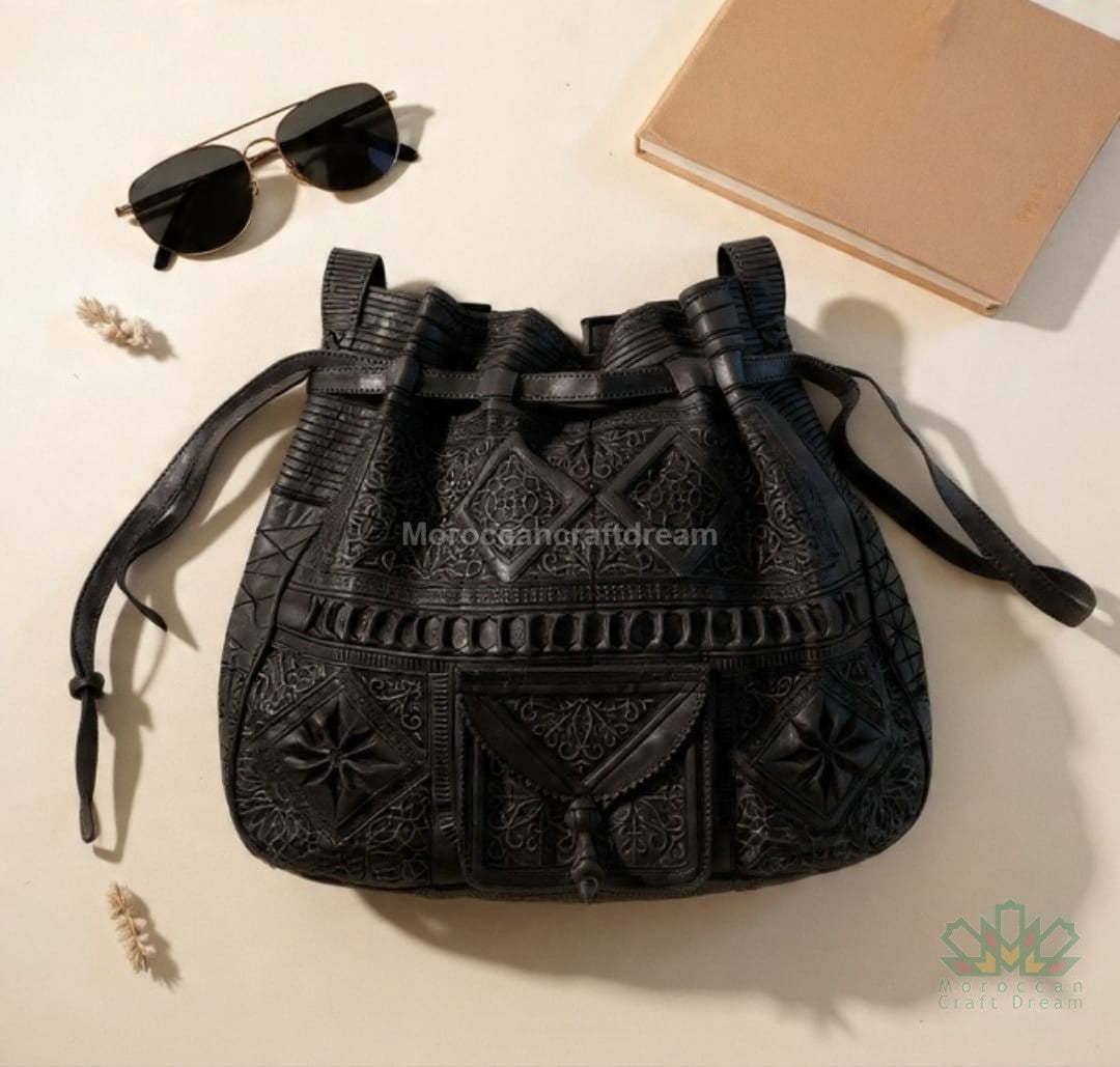 Black embroidered handbag with sunglasses and a notebook on a beige surface