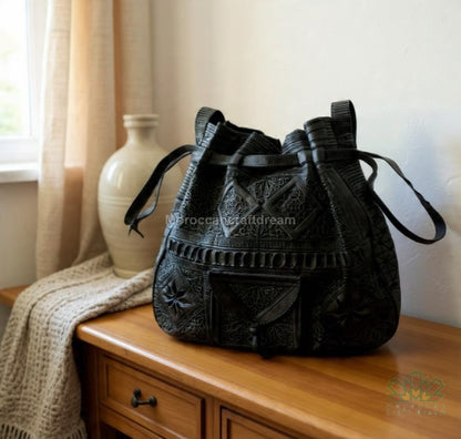 Black embroidered bag on a wooden surface with a vase and blanket in the background