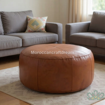 Brown leather ottoman in a living room setting with gray sofas and a patterned pillow.