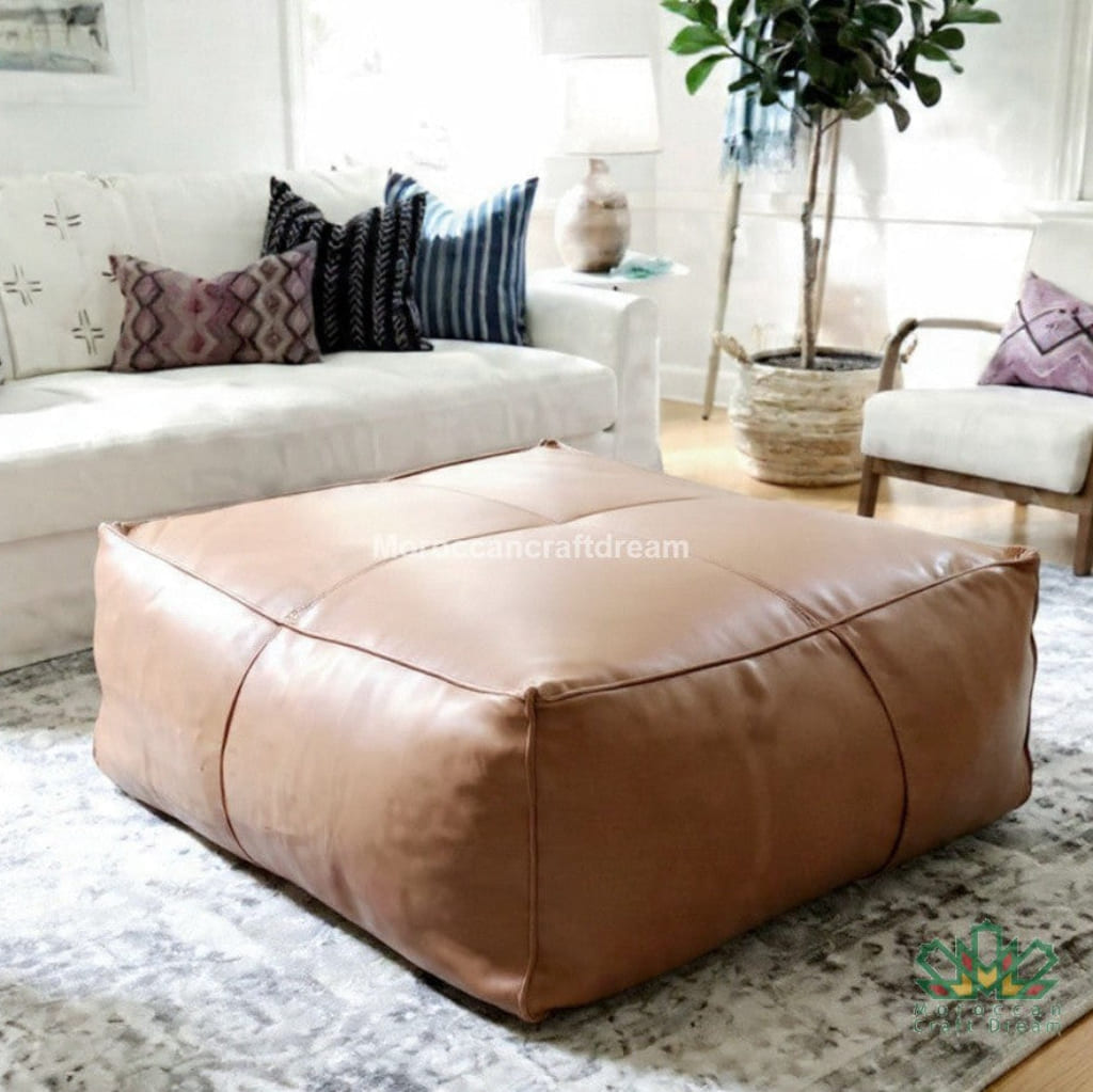 Brown leather ottoman in a living room setting with a white sofa and decorative pillows.