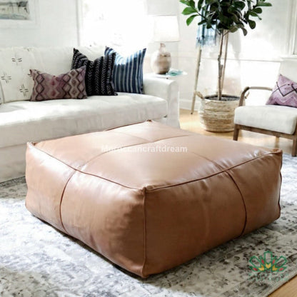 Brown leather ottoman in a living room setting with a white sofa and decorative pillows.