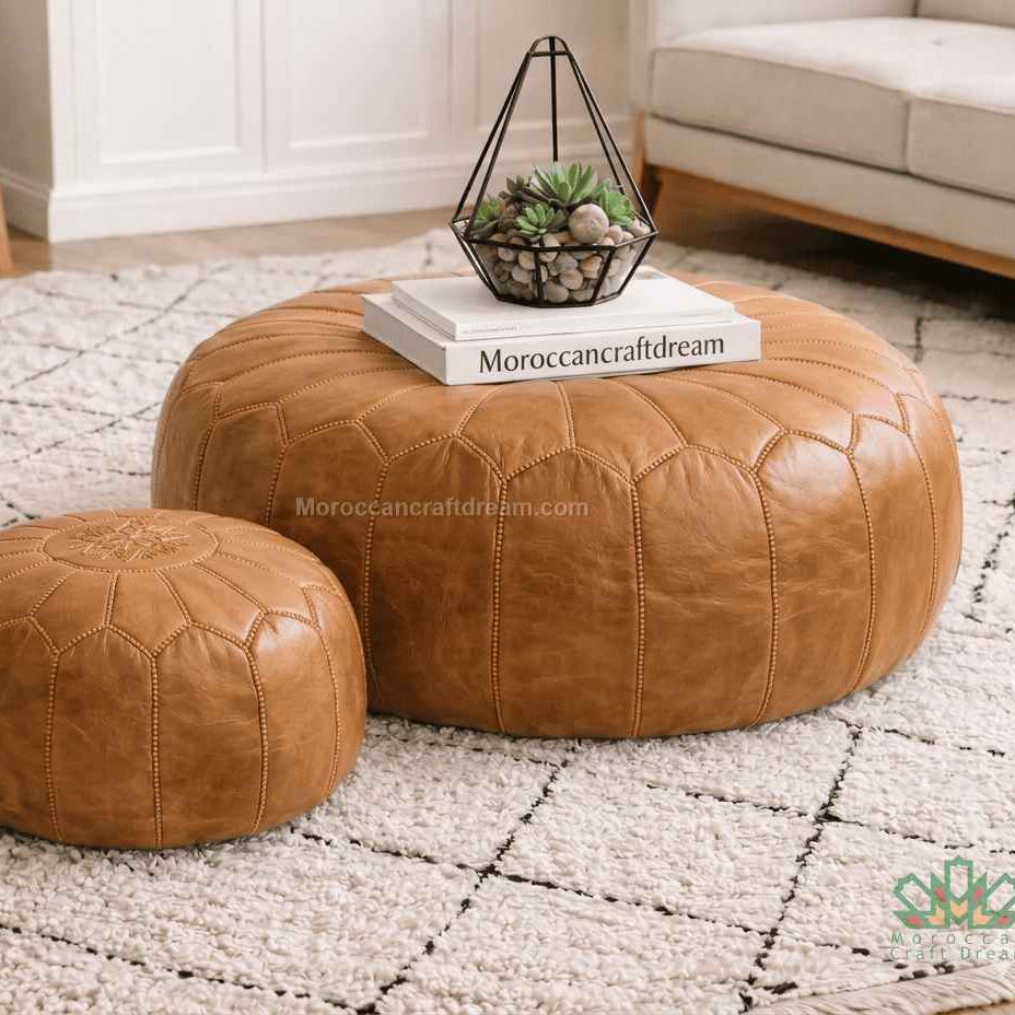 Two caramel leather ottomans on a textured rug with a book titled 'MoroccanCraftDream' on top.