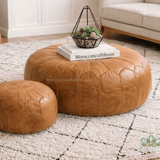 Two caramel leather ottomans on a textured rug with a book titled 'MoroccanCraftDream' on top.