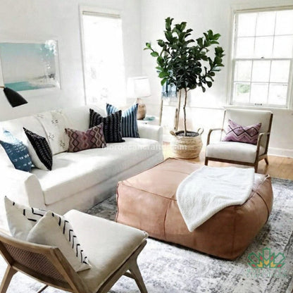 Living room with white sofa, light caramel ottoman, and decorative pillows.