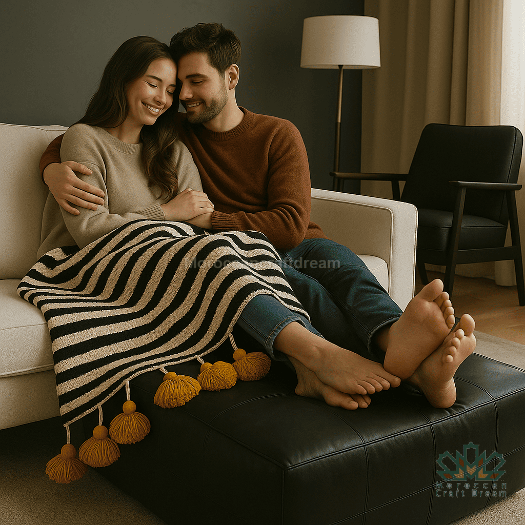 Couple sitting on a couch with a striped blanket, smiling and embracing.