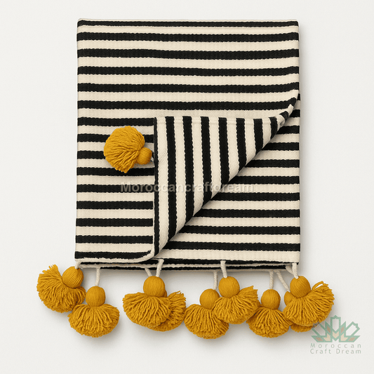 Black and white striped blanket with yellow pom-poms on a white background