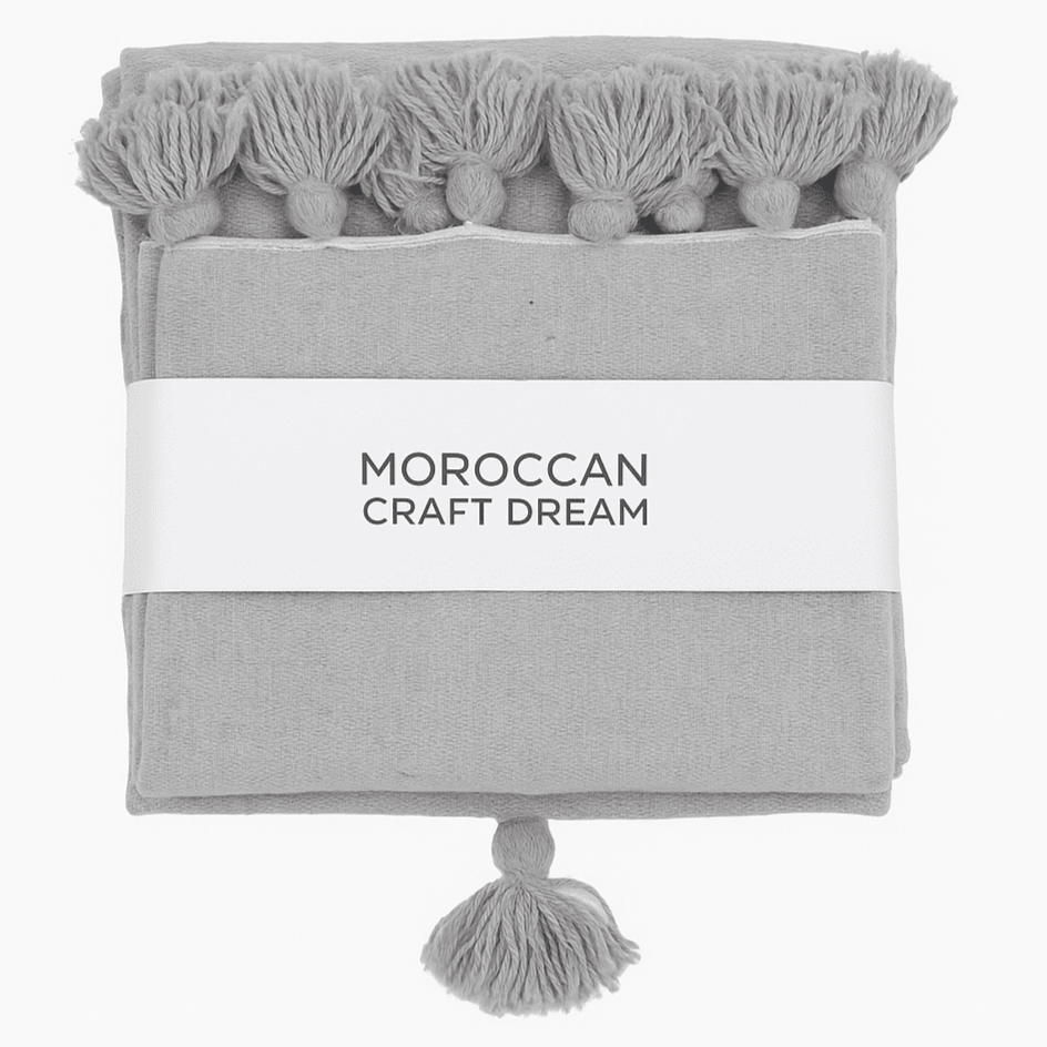 Gray towel with tassels and 'Moroccan Craft Dream' label on a white background