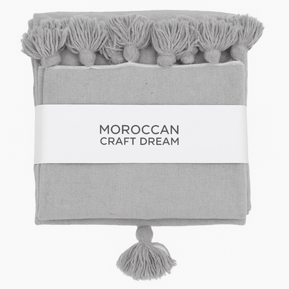 Gray towel with tassels and 'Moroccan Craft Dream' label on a white background
