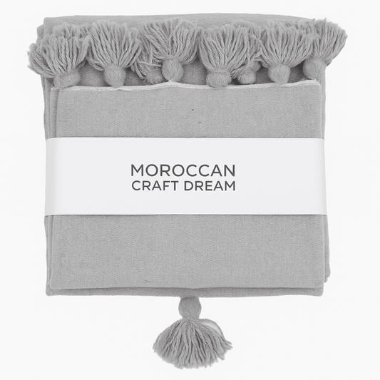 Gray towel with tassels and 'Moroccan Craft Dream' label on a white background