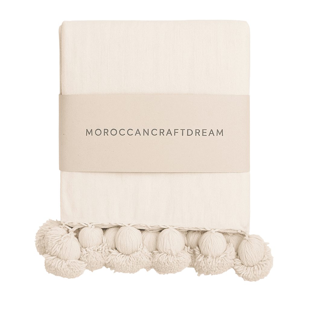 Beige throw blanket with pom-pom trim on a white background, featuring 'Moroccancraftdream' branding.