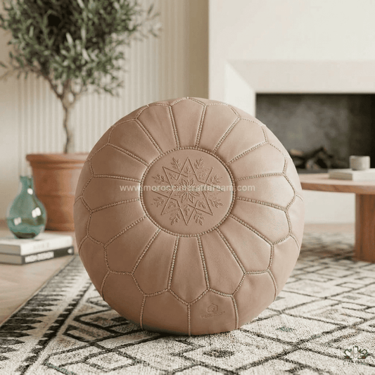 Blush Beige leather pouf on a patterned rug with a blurred indoor background