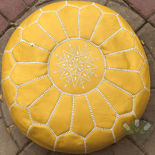 Mustard leather moroccan pouf with a star design on a stone pavement white stitching