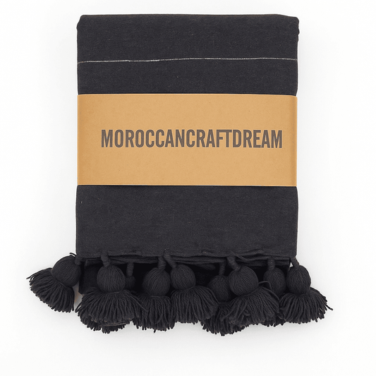 dark gray blanket with pom-pom trim and 'Moroccancraftdream' label on a white background