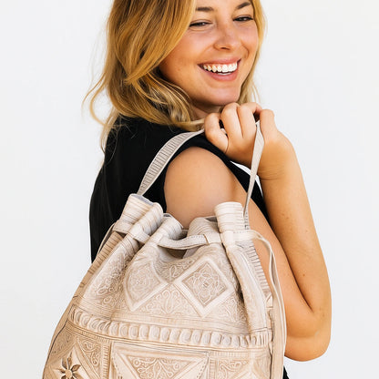 Woman holding a beige embroidered backpack against a white background
