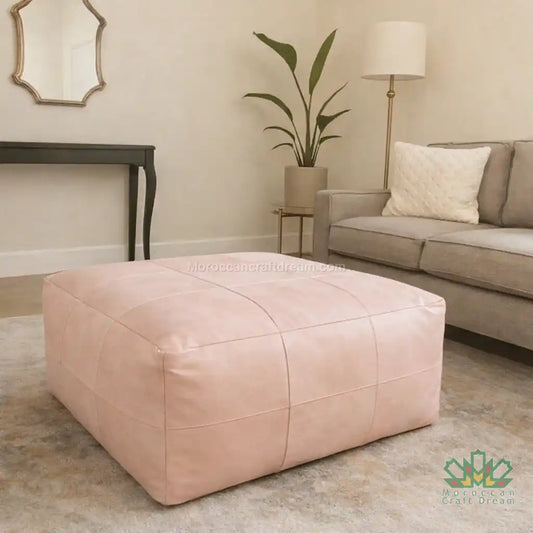 Pink ottoman in a living room setting with a sofa and plant.
