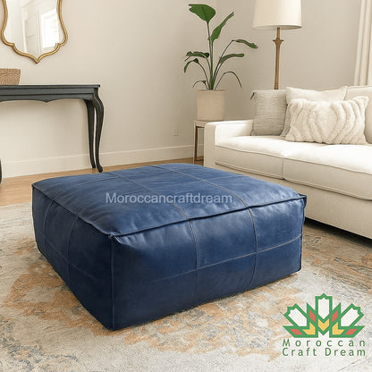 Blue leather ottoman in a living room setting with a beige sofa and decorative items.