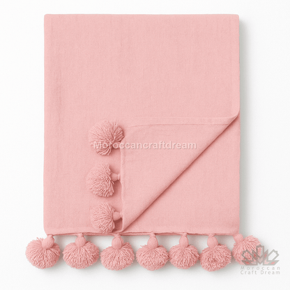 Pink blanket with pom-pom trim on a white background