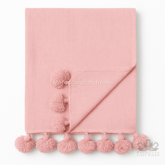Pink blanket with pom-pom trim on a white background